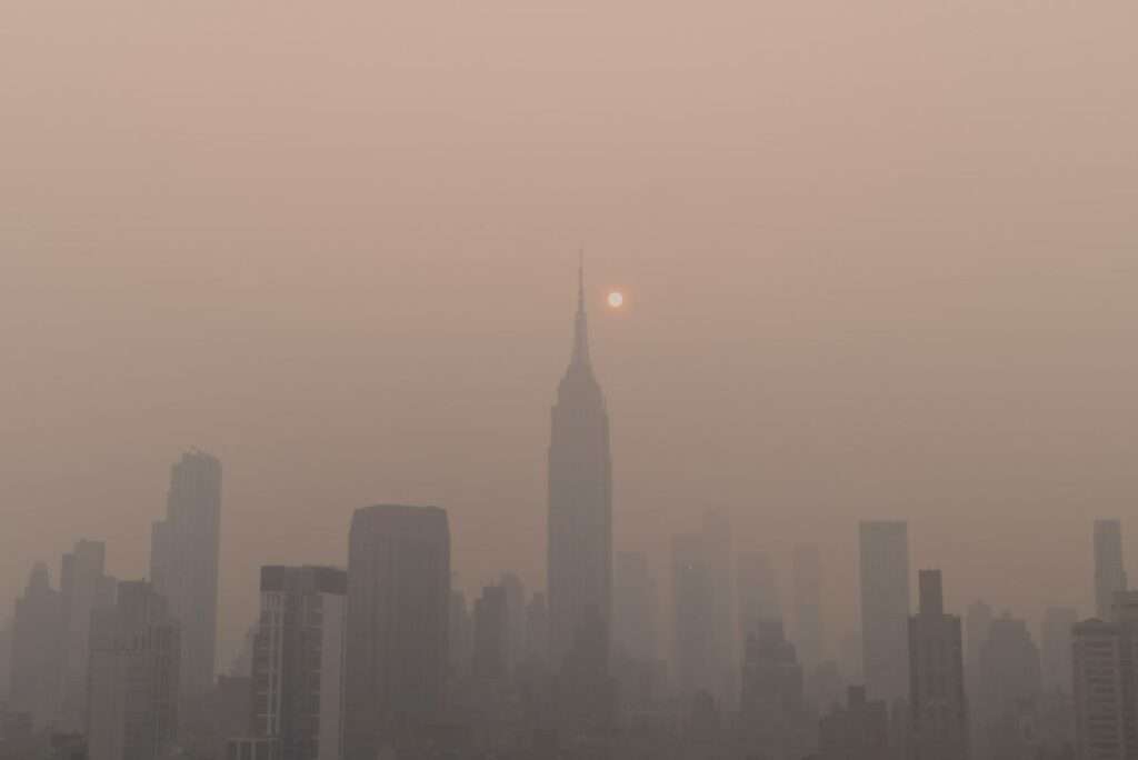 A photorealistic image of the New York City skyline partially obscured by a layer of smog, with the sun shining through in some areas.